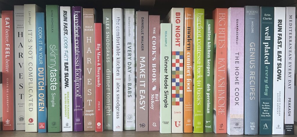 Variety of cookbooks lined up vertically on a bookshelf.