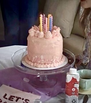 Pink pastel birthday cake on a glass cake stand with colorful candles and edible glitter