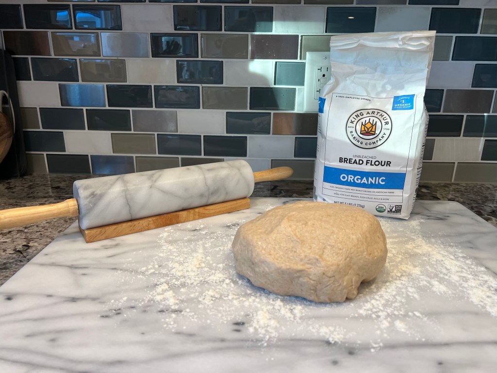 Oatmeal wheat bread dough after the first rise, resting on a pastry slab