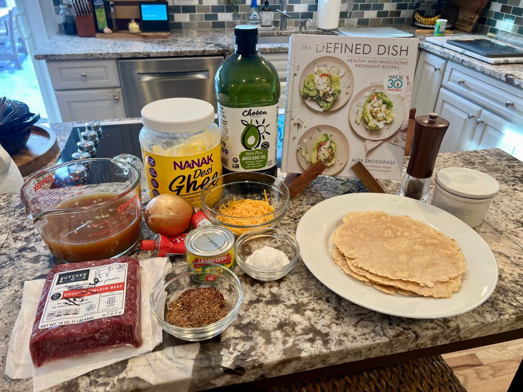 Prep ingredients for beef enchiladas with The Defined Dish cookbook on the counter