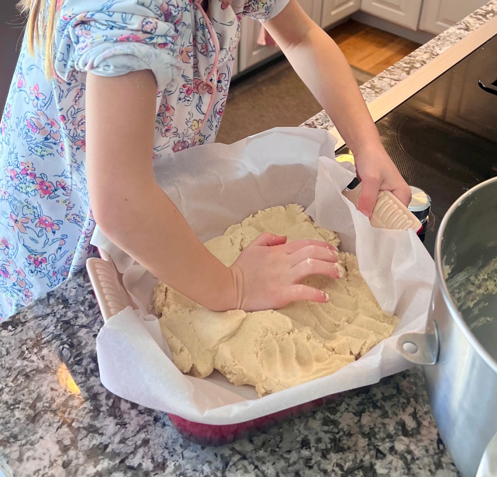 Hands pressing vanilla bean shortbread dough into a square baking pan.