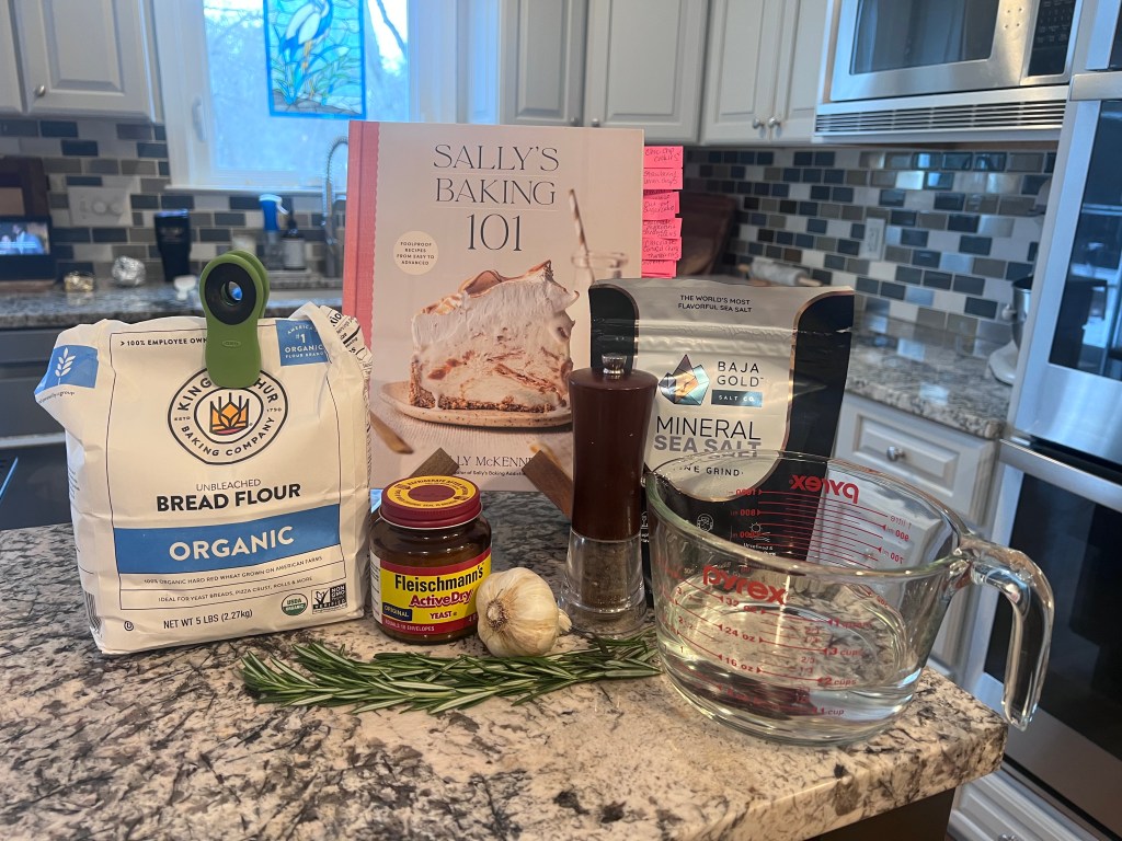 Sally’s Baking 101 cookbook for rosemary garlic bread recipe with ingredients on kitchen counter