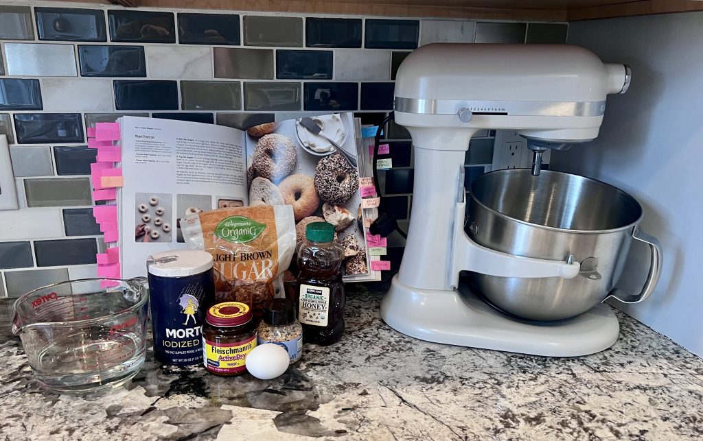 Sally’s Baking 101 cookbook open to the homemade bagel recipe with stand mixer and ingredients arranged on the counter