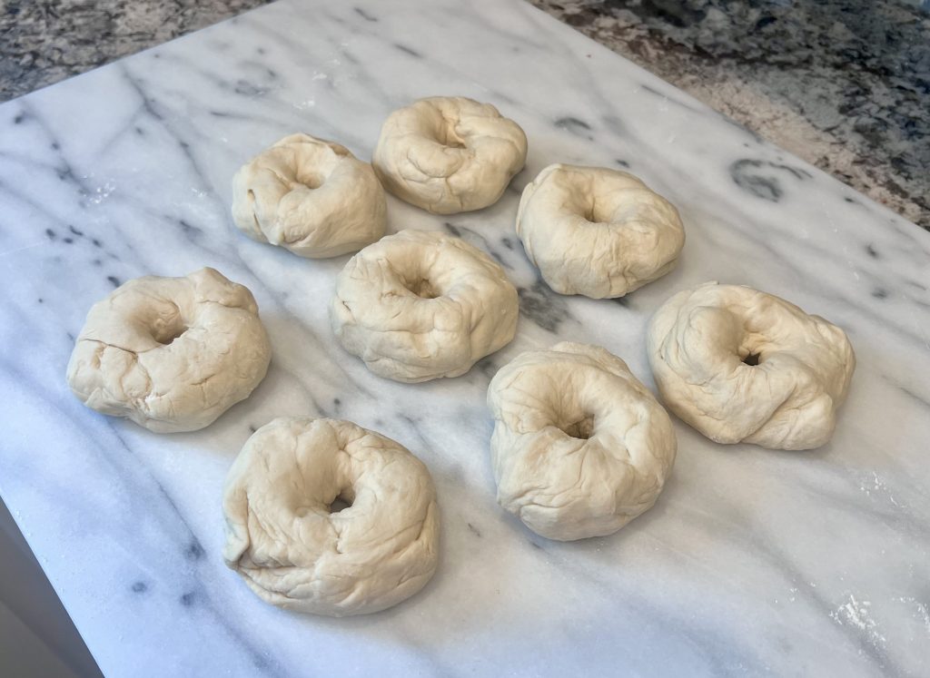 Shaped homemade bagels resting on a baking sheet before boiling and baking