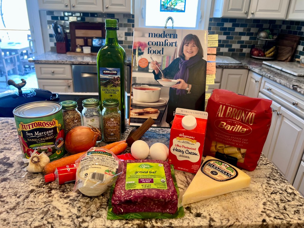Ina Garten’s Modern Comfort Food cookbook on the counter with ingredients for baked rigatoni ragu arranged beside it