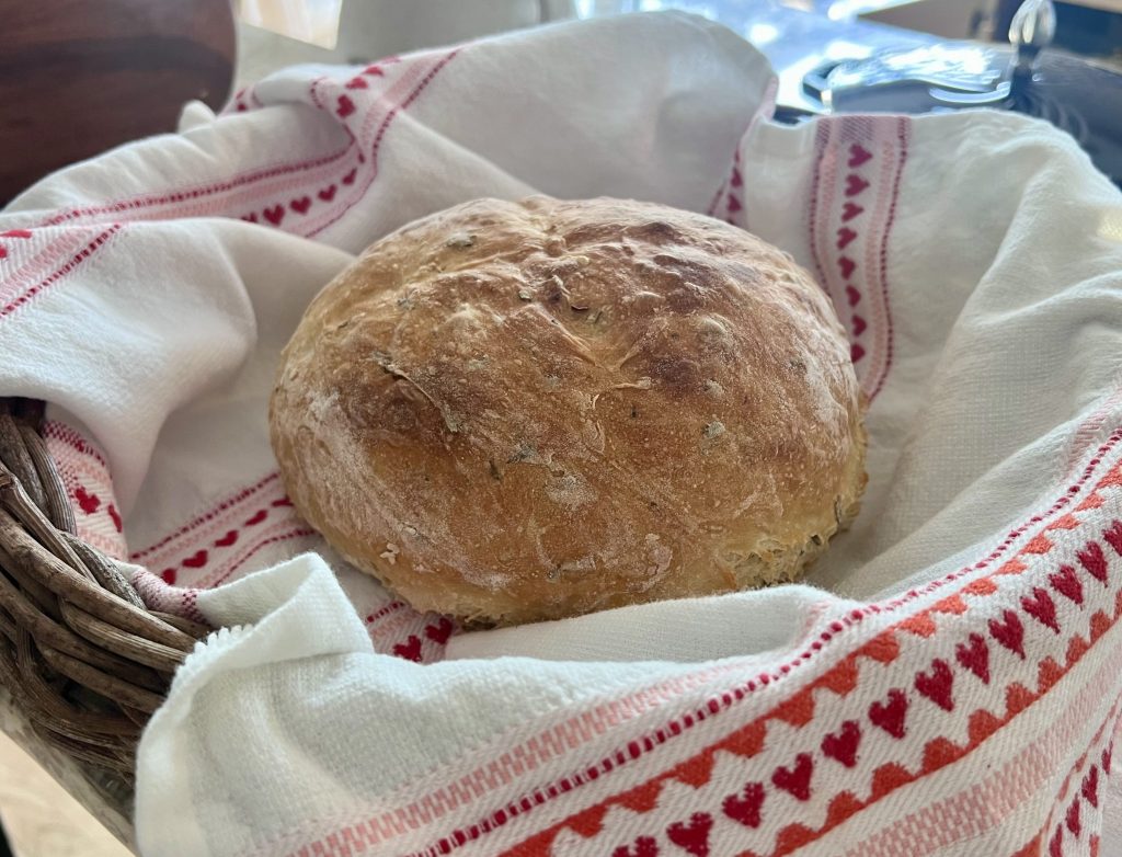 Whole rosemary garlic bread loaf in bread basket lined with decorative towel, styled for gifting.