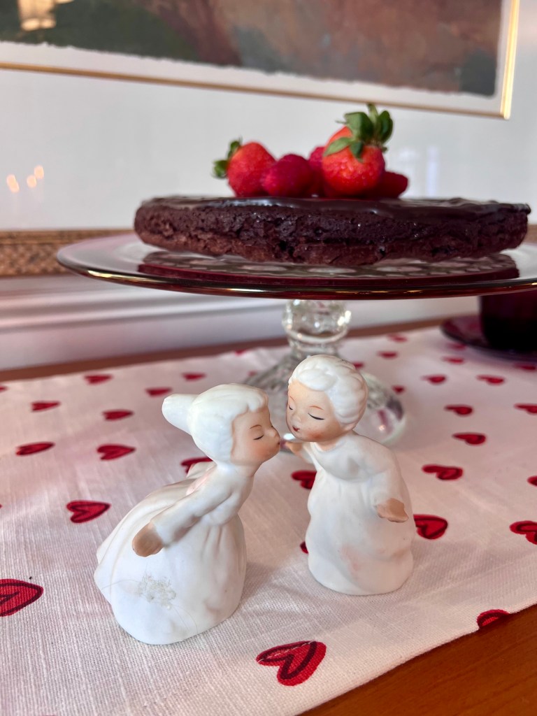 Porcelain statues kissing in front of flourless chocolate cake on a cake stand. 