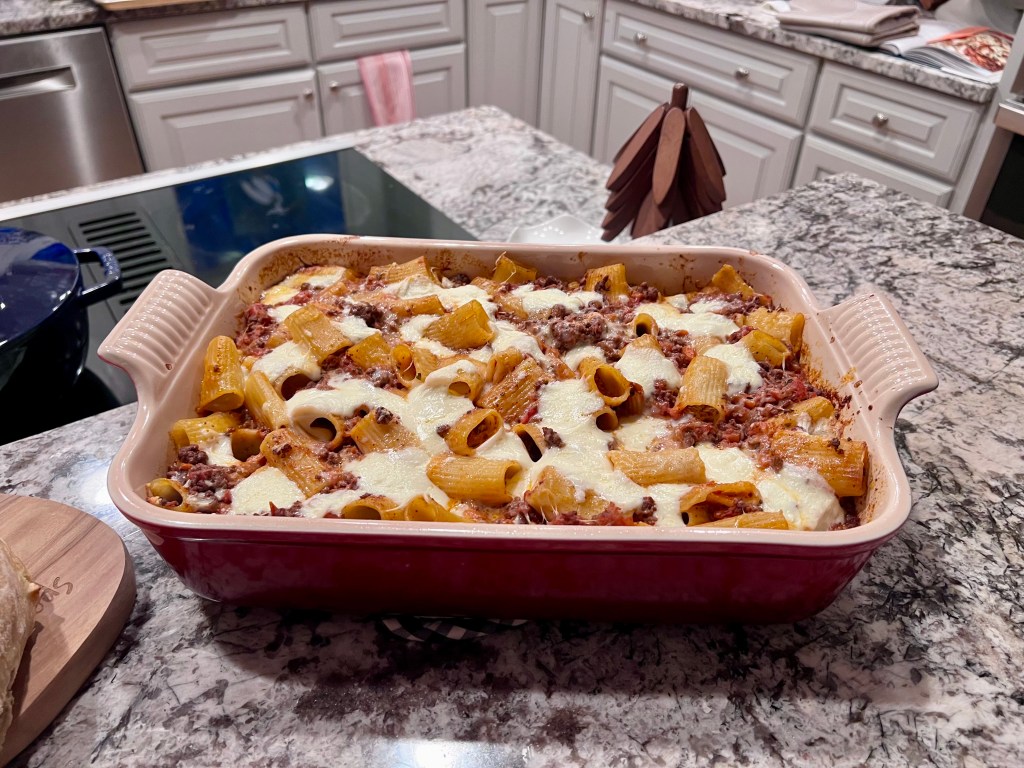 Baked rigatoni with beef ragu in a white ceramic baking dish, topped with melted cheese.