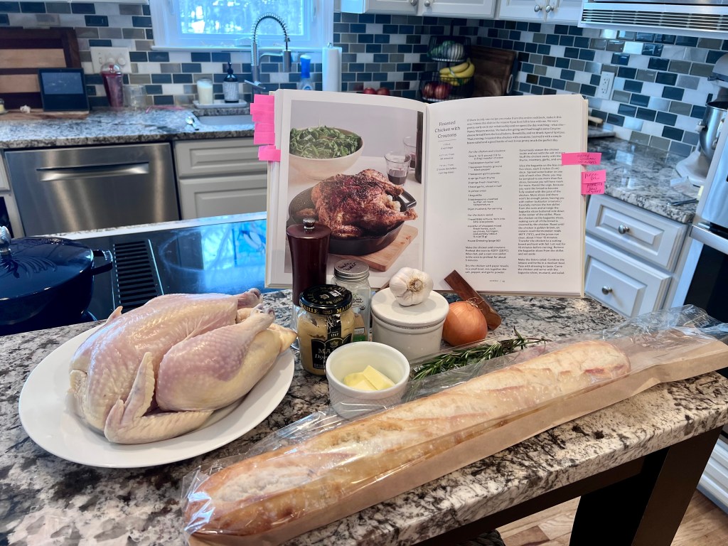 Open copy of “It’s Not Complicated” by Katie Lee Biegel with ingredients for roast chicken arranged on the kitchen counter