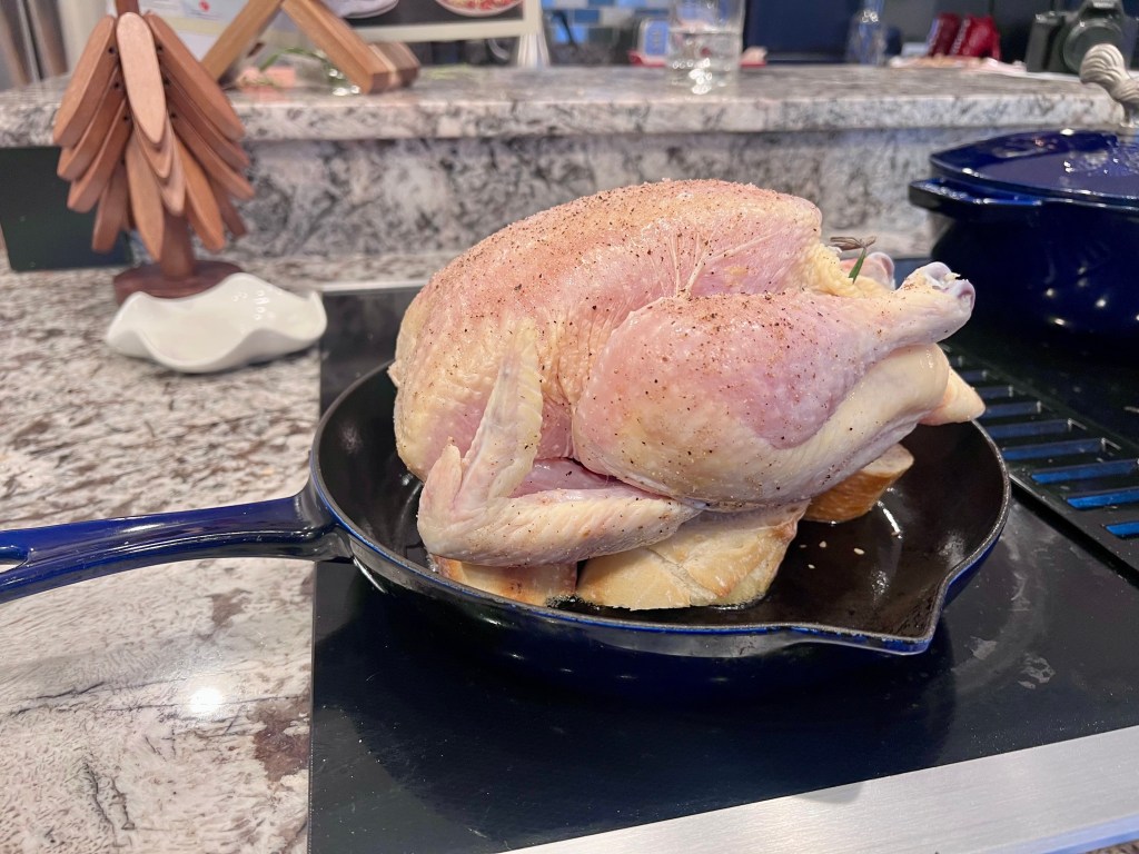 Whole raw chicken placed on buttered baguette slices in a cast iron skillet before roasting