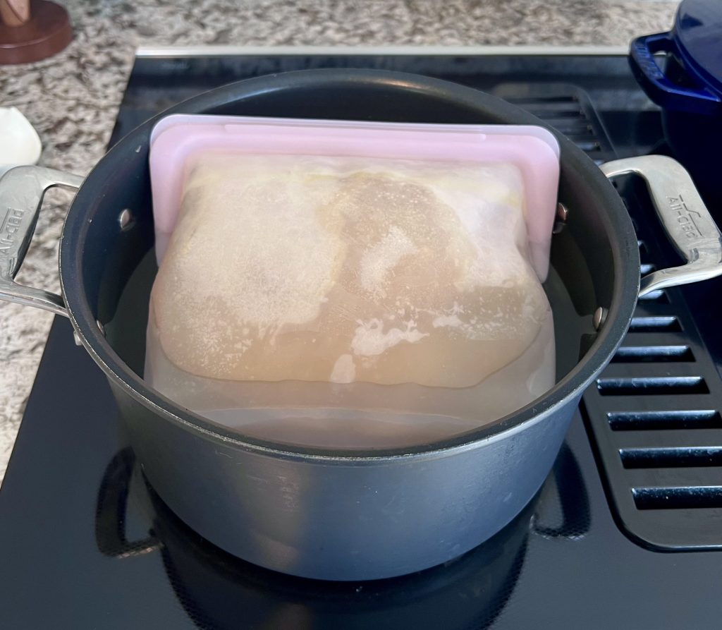 Frozen homemade chicken stock in a Stasher bag being warmed.