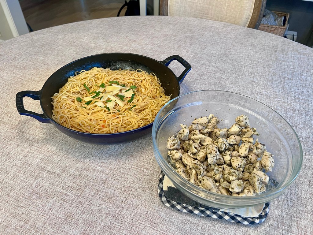 Garlic butter pasta in a roasting pan and Italian seasoned chicken bites in a serving bowl set on a kitchen table before dinner.