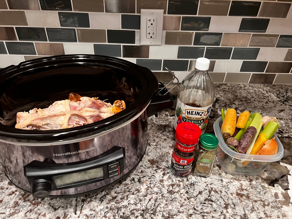 Chicken bones in a crock pot with chicken stock ingredients next to it.