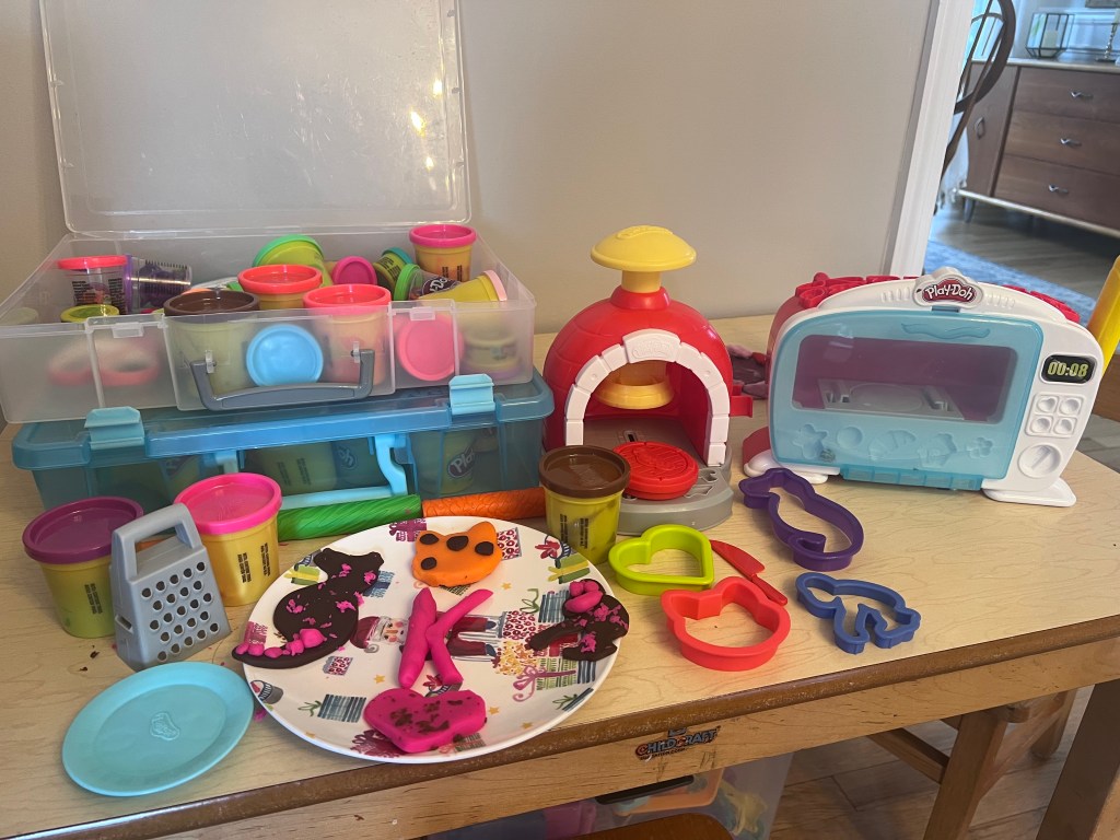 Plate of decorated Play-Doh cookies on a child’s table surrounded by cookie cutters and Play-Doh tools.