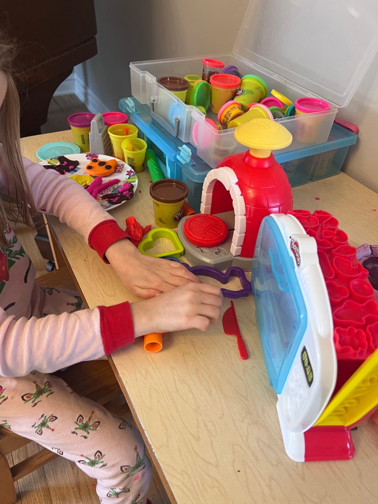 Rolling out colorful Play-Doh with a small rolling pin on a kids table.