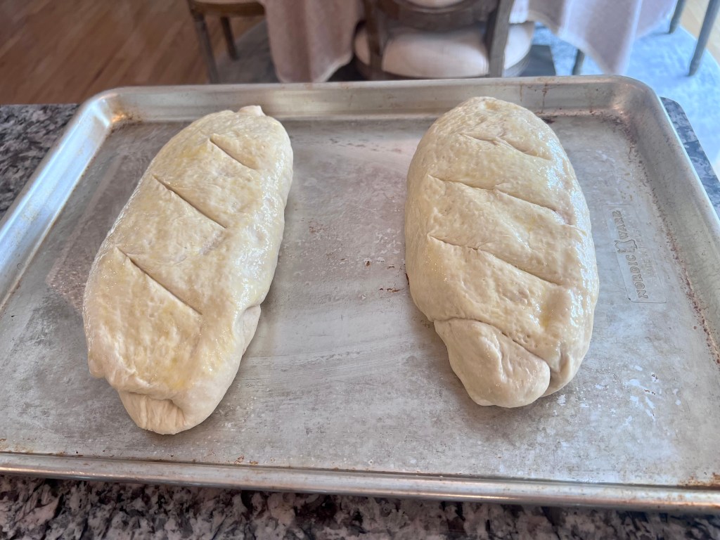 Shaped homemade French bread dough loaves scored and ready to bake on a sheet pan.