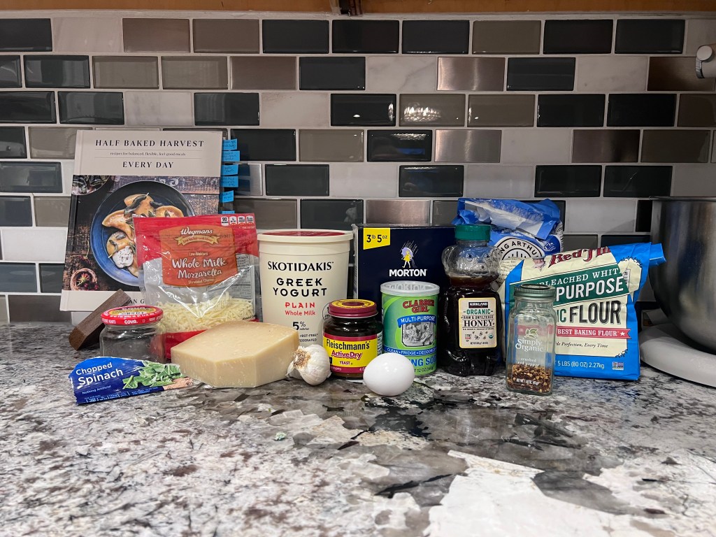 Ingredients for homemade spinach artichoke pretzel with the Half Baked Harvest Every Day cookbook on the kitchen counter.