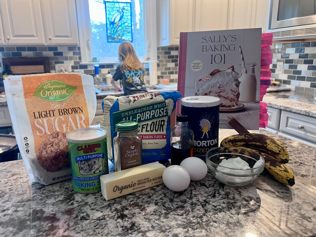 Cookbook and banana bread ingredients arranged on kitchen counter before baking