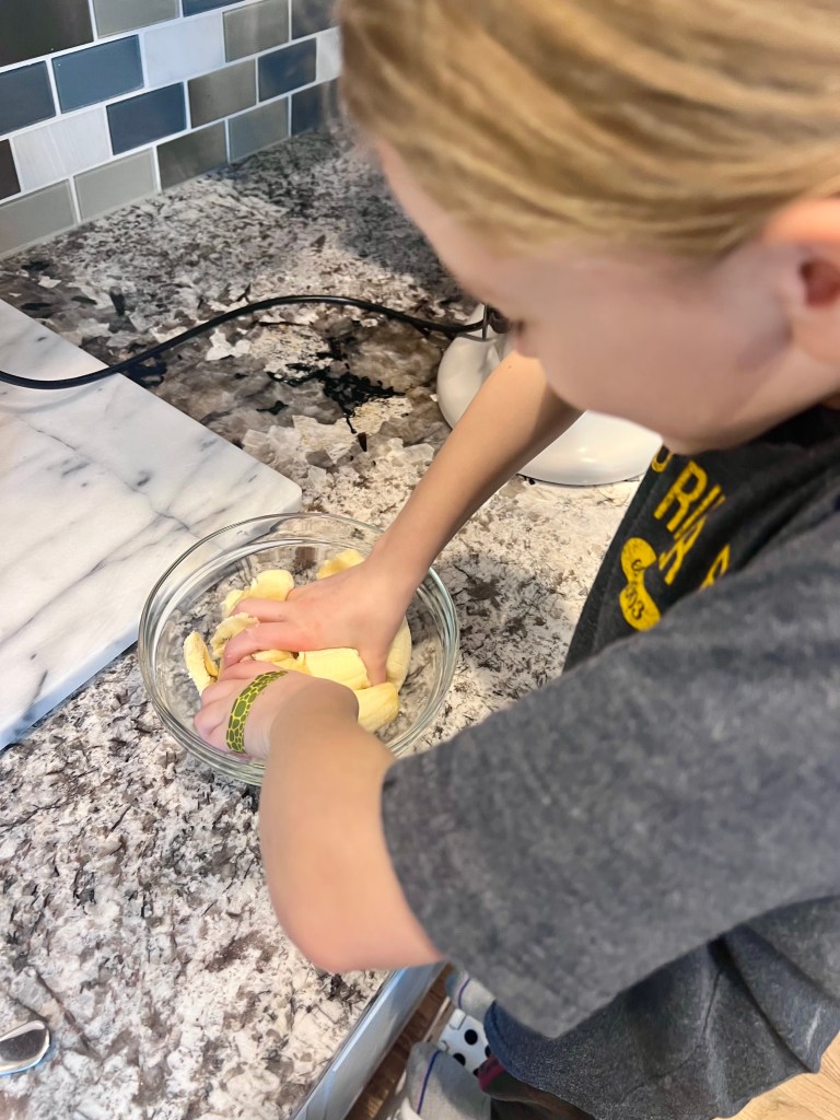 Child mashing ripe bananas in a mixing bowl while helping make homemade banana bread