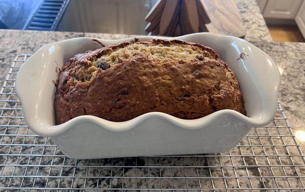 Freshly baked banana bread loaf cooling in a bread pan on a wire rack on the kitchen counter