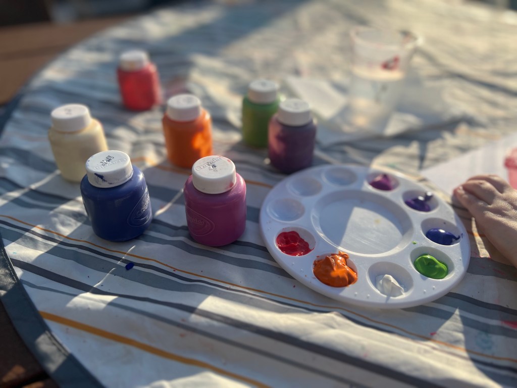 Paint brushes, paint tray, paper, and water cup set up on outdoor table for kids painting activity
