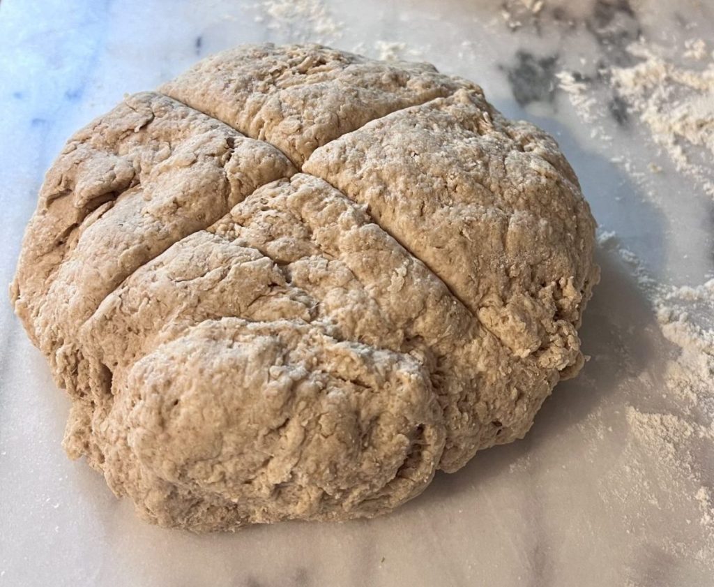 Irish soda bread dough shaped and scored on a pastry slab before baking