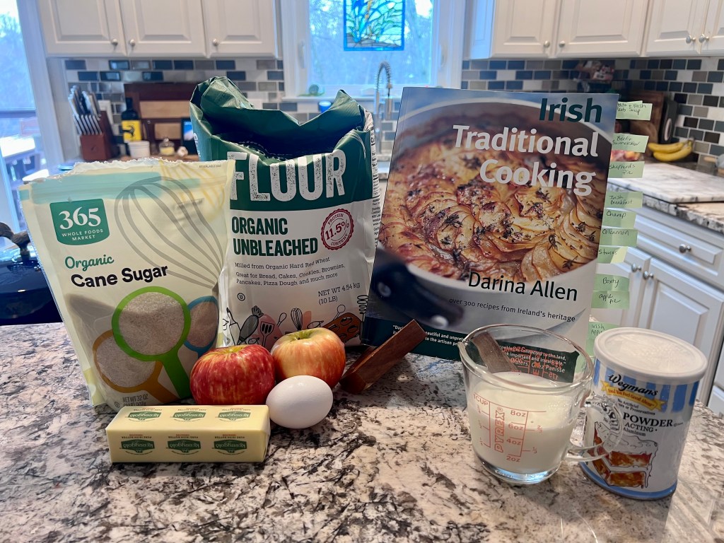 Unopened Irish Traditional Cooking cookbook by Darina Allen with ingredients for Irish apple cake arranged on a kitchen counter for St. Patrick’s Day baking