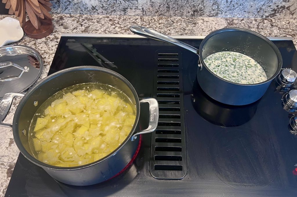 Potatoes boiling in one pot and milk with parsley warming in another pot on the stove for making parsley champ