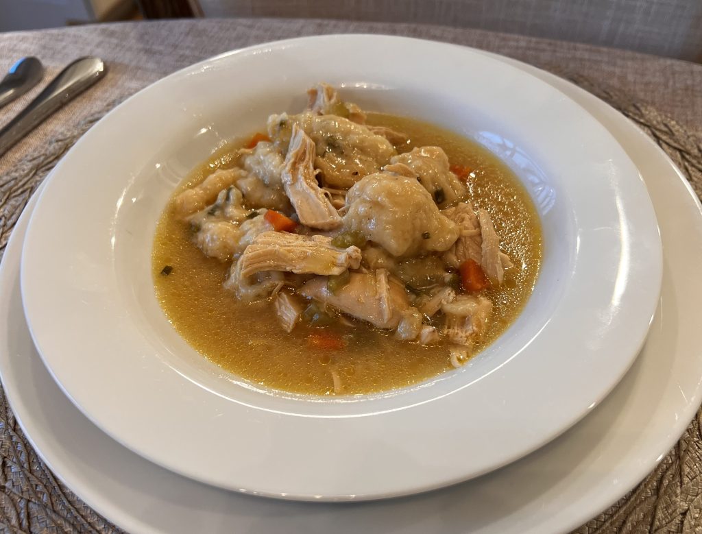 Bowl of chicken soup with yogurt dumplings, carrots, and celery, plated and ready to eat.